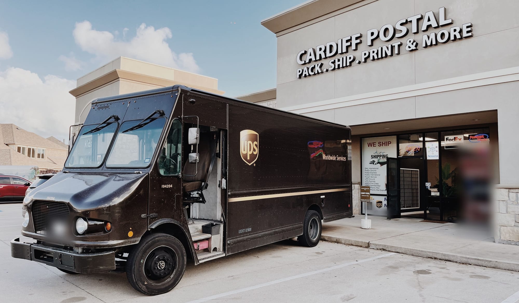 The Cardiff Postal storefront on FM 1463 with its lit sign, Pack . Ship . Print & More, and a brown UPS package truck parked at the entrance